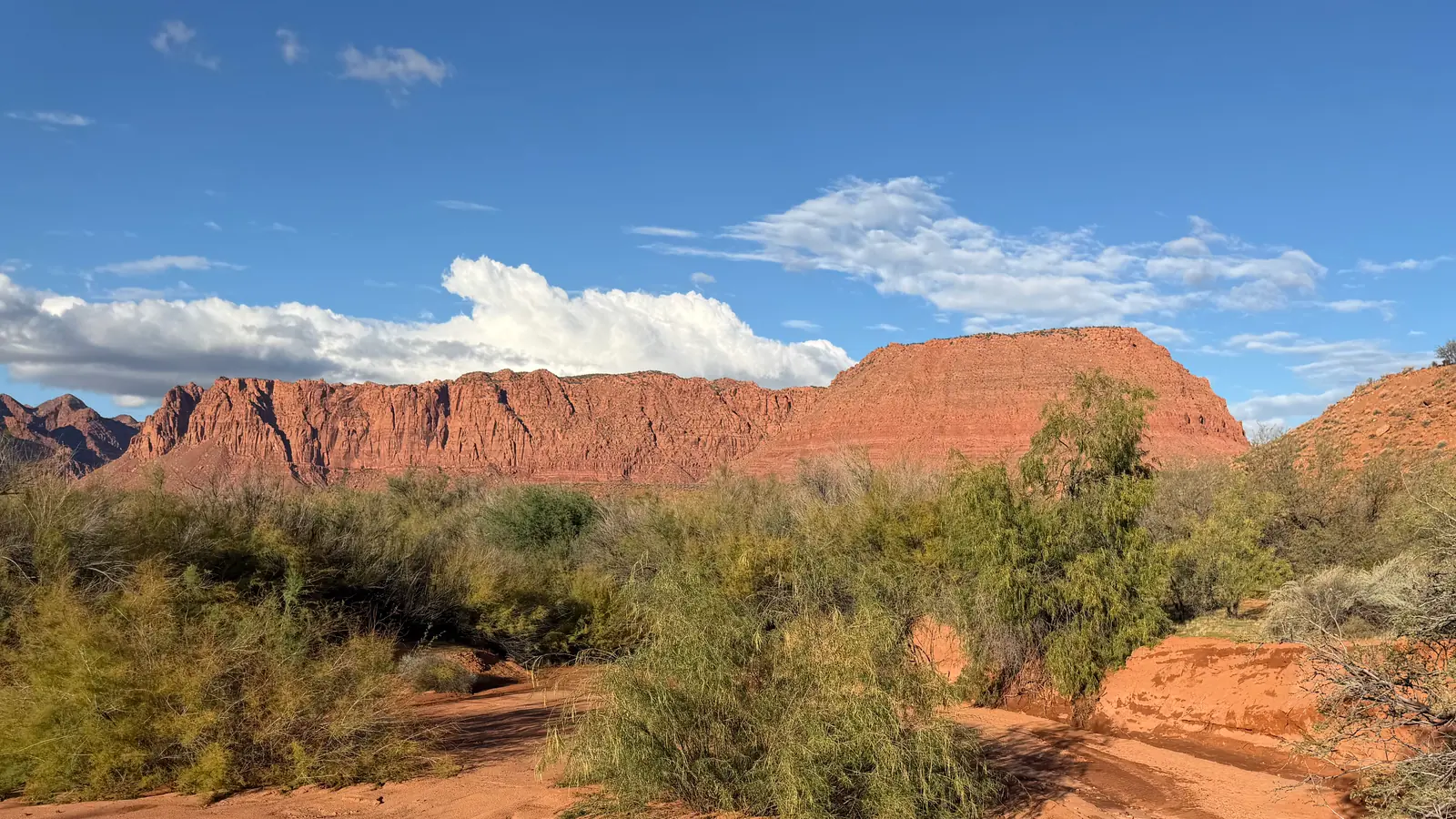 Desert wash with green brush below red sandstone cliffs near Ivins, Utah