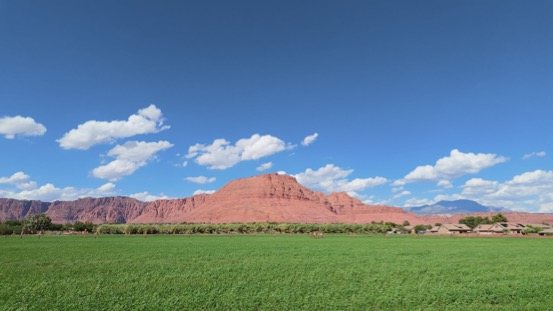 Green field below a red mountain under blue sky near Ivins, Utah